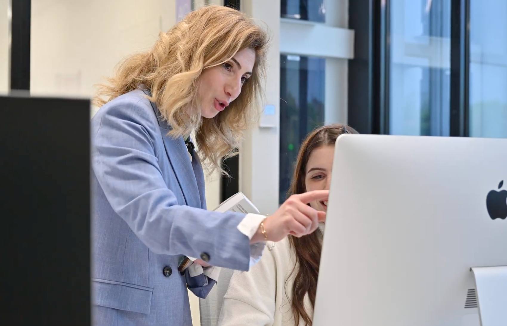 A mentor pointing at a screen while reviewing a student's work